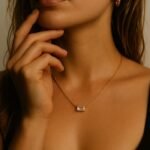 Personne avec un collier en or, pendentif rectangulaire transparent, boucles d'oreilles dorées.